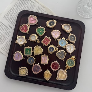 May include: A collection of vintage-style watch faces in various shapes, including hearts, stars, and squares, with gold-toned metal frames. The watch faces feature different colored dials and are arranged on a dark wooden tray.