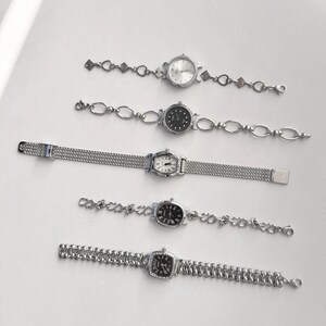 May include: Five silver-toned wristwatches with various band designs and watch faces. The watches feature round, oval, and square faces with different dial colors, including white and black. The bands include chain-link and mesh styles, offering a variety of elegant options.