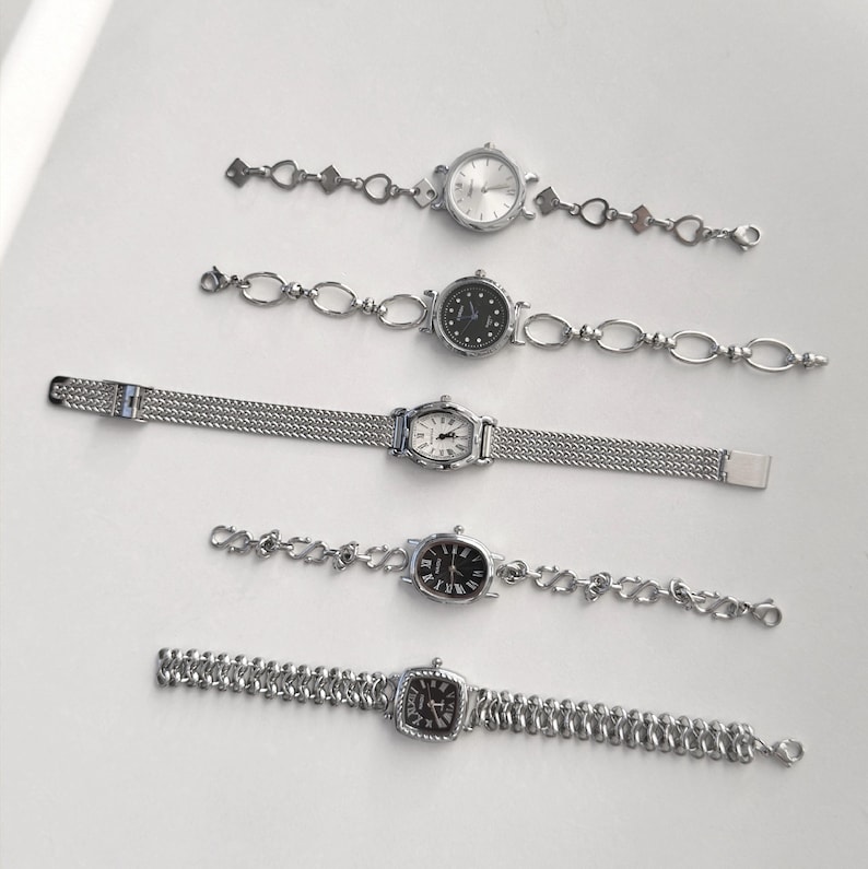 May include: Five silver-toned wristwatches with various band designs and watch faces. The watches feature round, oval, and square faces with different dial colors, including white and black. The bands include chain-link and mesh styles, offering a variety of elegant options.
