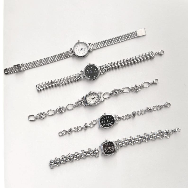 May include: Five silver-toned wristwatches with various band designs and watch faces. The watches have round, oval, and square faces with different dial colors. The bands include mesh, beaded, and chain-link styles. The watches are displayed on a white surface.