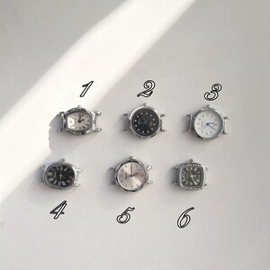 May include: Six small, silver-toned wristwatches with various face designs. The watches have different shapes, including oval and square, and feature Roman numerals and hands. The watch faces are white, black, and silver, with some having a textured appearance.