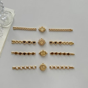 May include: An assortment of vintage-style gold-toned watches and watch bands. The bands feature chain links, brown gemstone accents, and white pearl accents. The watch faces are round and oval, with intricate detailing.