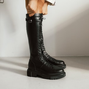 May include: Black leather knee-high boots with a lace-up front and a chunky platform sole.