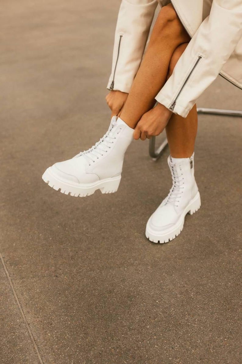 Puede incluir: Botas blancas de cuero con cordones y suela gruesa blanca. Las botas tienen una cremallera lateral y las lleva una persona.