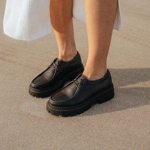 May include: A pair of black leather lace-up shoes with thick soles. The shoes have a chunky platform and a rounded toe.