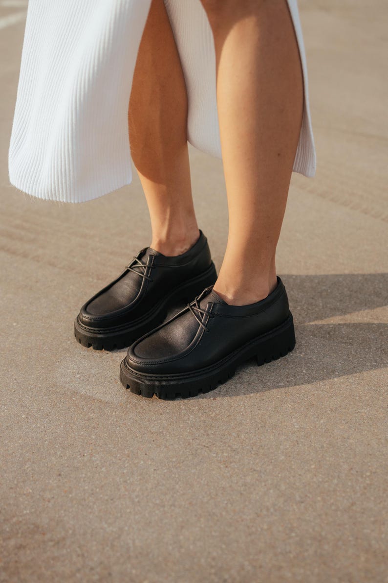 May include: A pair of black leather lace-up shoes with thick soles. The shoes have a chunky platform and a rounded toe.