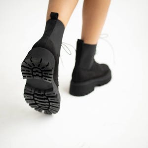 May include: Black suede ankle boots with a chunky platform sole and lace-up closure. The boots have a textured rubber outsole.