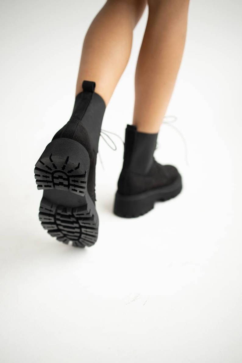 May include: Black suede ankle boots with a chunky platform sole and lace-up closure. The boots have a textured rubber outsole.