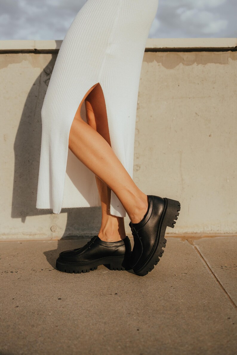 May include: A person wearing a white maxi dress with a side slit and black leather platform shoes.