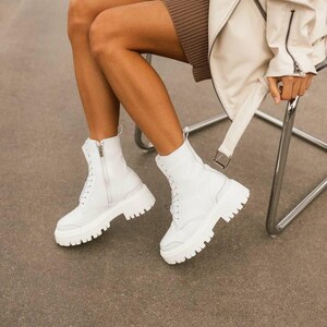 Puede incluir: Botas blancas de cuero con suela de plataforma gruesa y cierre de cordones.