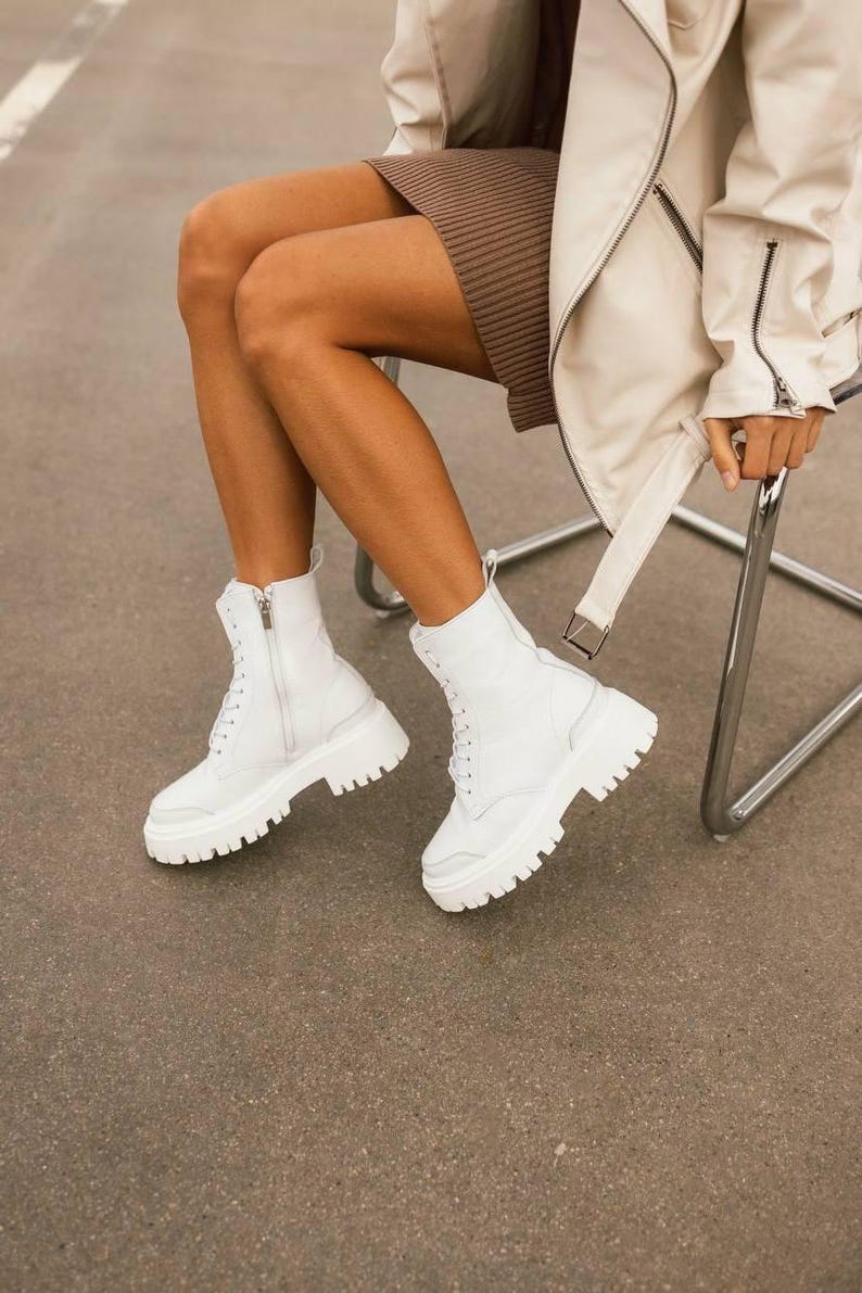 Puede incluir: Botas blancas de cuero con suela de plataforma gruesa y cierre de cordones.
