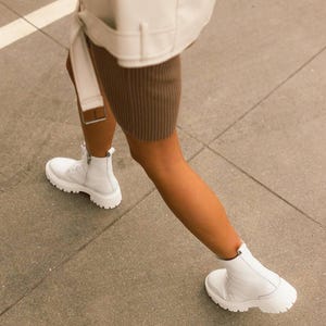 Puede incluir: Botas blancas de cuero con cordones y suela gruesa. Las botas las lleva una persona que lleva una falda marr&oacute;n y una chaqueta blanca.