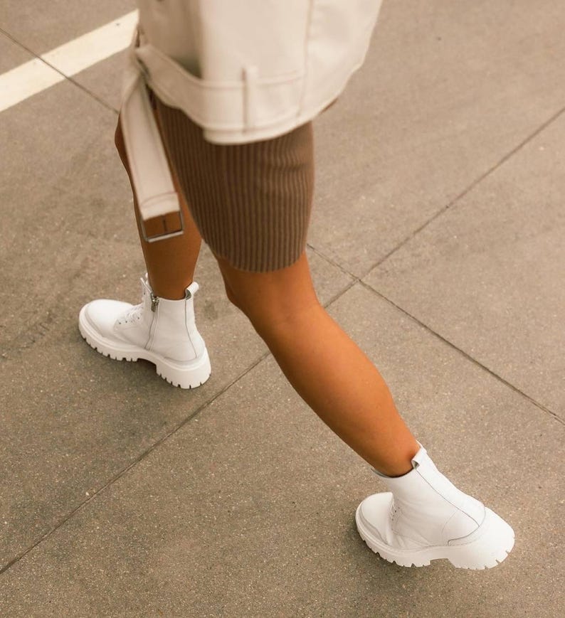 Puede incluir: Botas blancas de cuero con cordones y suela gruesa. Las botas las lleva una persona que lleva una falda marr&oacute;n y una chaqueta blanca.