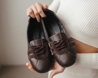 May include: A pair of brown leather shoes with white stripes and laces. The shoes are held in a person's hands.