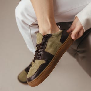 Pair of khaki leather and olive suede sneakers with wide toes, placed on a light gray surface, showcasing the minimalist design and TEP sole