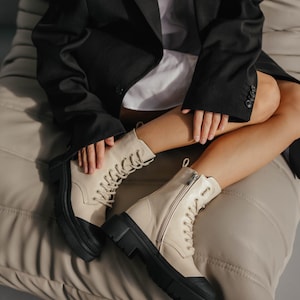May include: A pair of cream-colored leather boots with black soles and laces. The boots have a chunky platform heel and a zipper on the side.