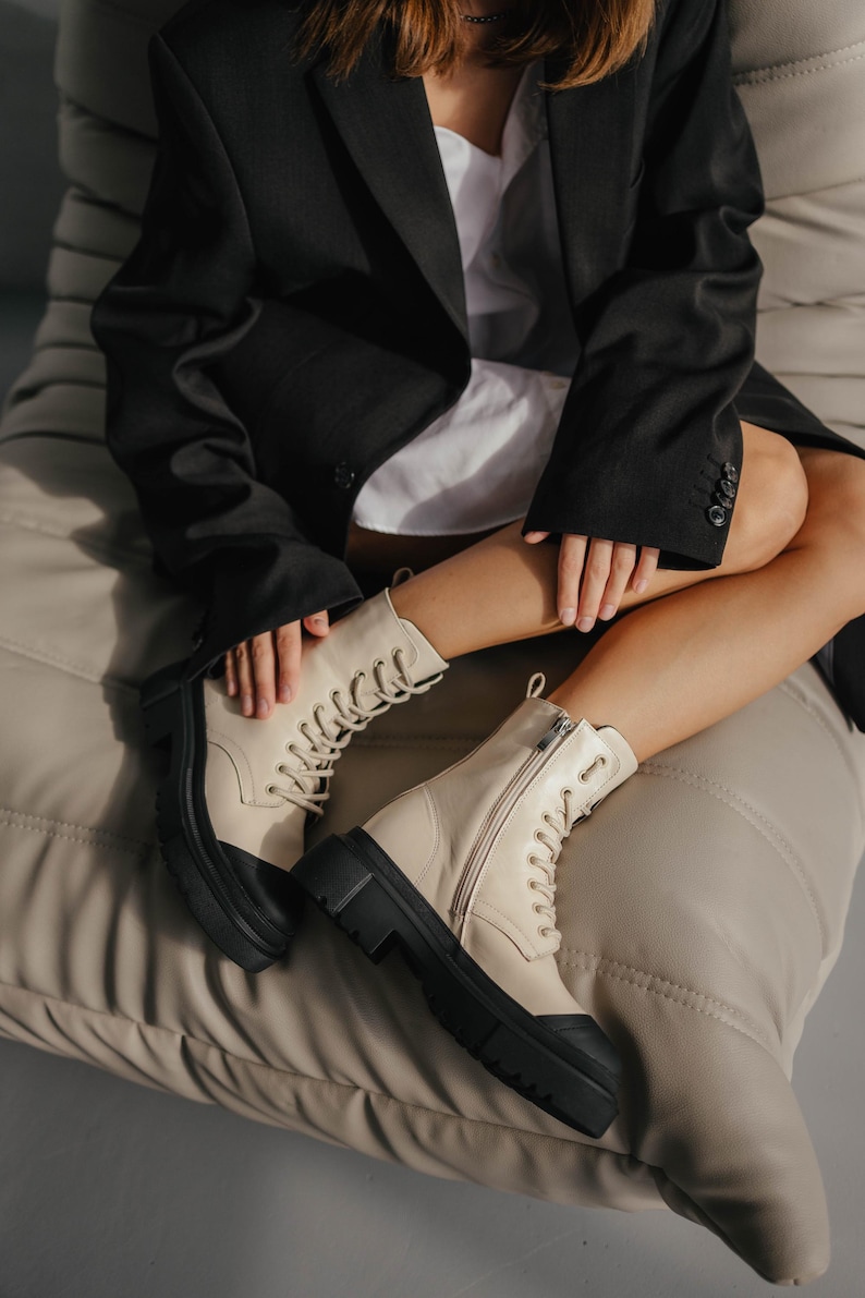 May include: A pair of cream-colored leather boots with black soles and laces. The boots have a chunky platform heel and a zipper on the side.