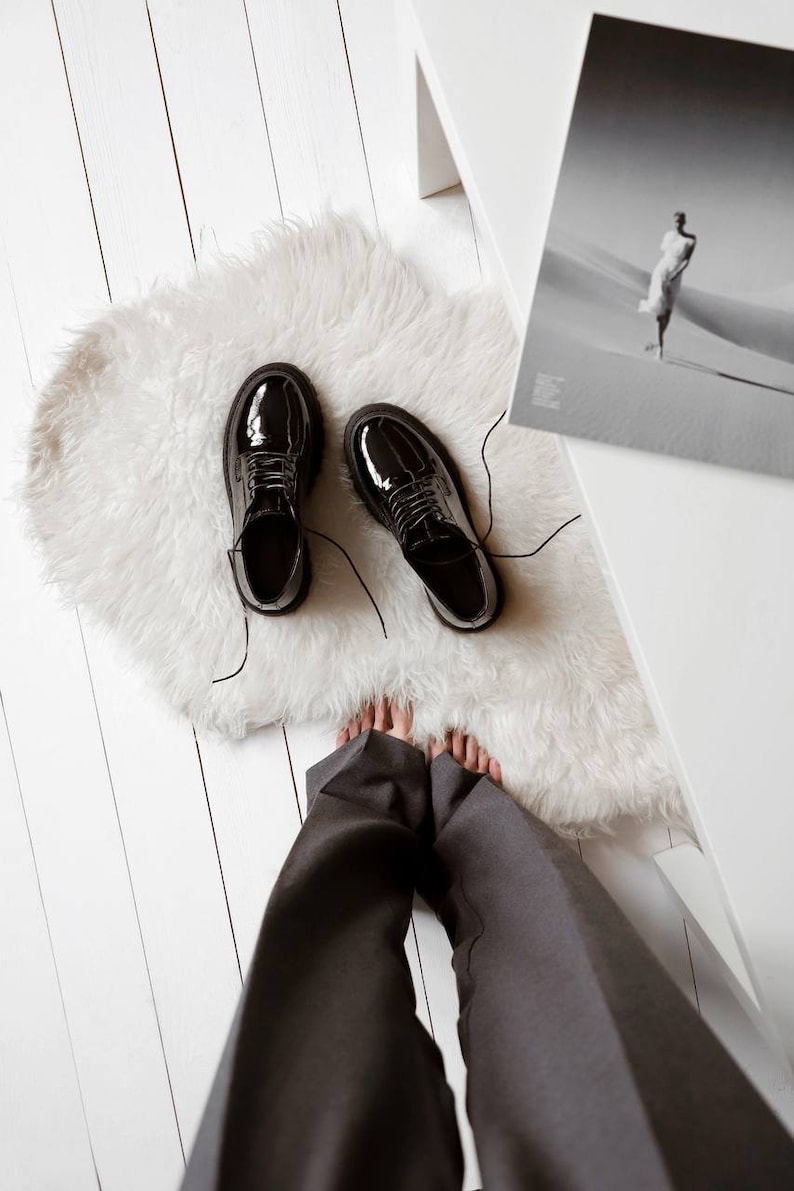 May include: A pair of black patent leather oxford shoes with thick, lugged rubber soles and black laces. The shoes feature a glossy, reflective finish, a rounded toe box, and a low-cut silhouette that exposes the ankle area, presented from a top-down view.