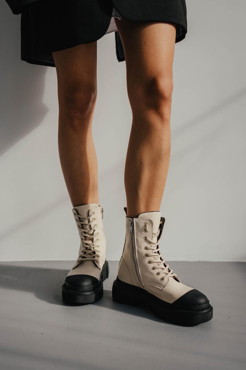 May include: A pair of cream-colored leather boots with black laces and a black platform sole. The boots have a zipper on the side and a rounded toe.