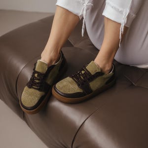 Top-down view of women's khaki leather sneakers with olive suede accents, brown laces tied, highlighting the wide toe design and perforation detail