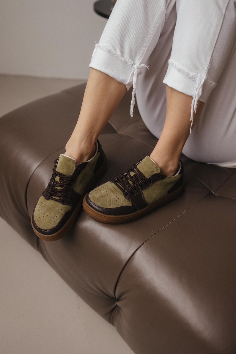 Top-down view of women's khaki leather sneakers with olive suede accents, brown laces tied, highlighting the wide toe design and perforation detail