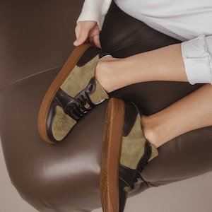 Side view of khaki leather and olive suede sneakers with a wide rounded toe, showcasing the natural leather texture and TEP sole, on a light gray floor