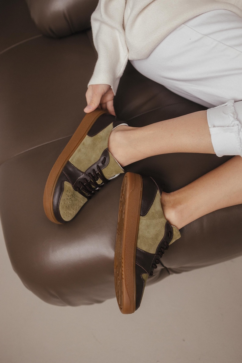 Side view of khaki leather and olive suede sneakers with a wide rounded toe, showcasing the natural leather texture and TEP sole, on a light gray floor