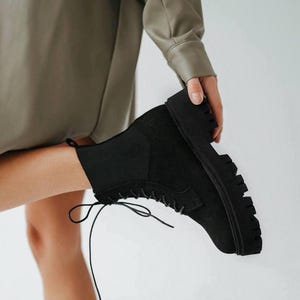 May include: Black lace-up ankle boots with a chunky platform sole. The boots are made of suede and have a zipper on the inside of the ankle.