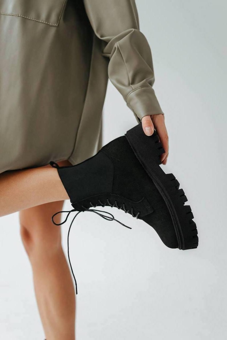 May include: Black lace-up ankle boots with a chunky platform sole. The boots are made of suede and have a zipper on the inside of the ankle.