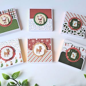 May include: Six Christmas gift card holders with festive designs. Each holder has a unique pattern, featuring Santa Claus, reindeer, and holiday motifs. The holders are square-shaped with a pocket, perfect for the holiday season.