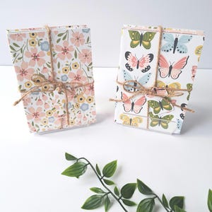 May include: Two sets of note cards, one with a floral pattern and the other with a butterfly pattern, are tied with twine and displayed on a white surface.