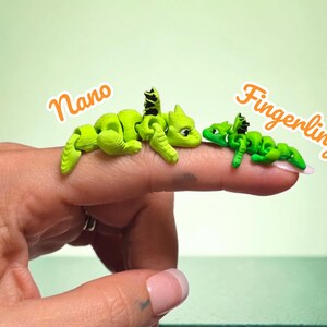 May include: Two small articulated dragon figurines in bright green with black wing details. The larger dragon is labeled Nano and the smaller one is labeled Fingerling. Both figures feature segmented bodies and are positioned on a finger.