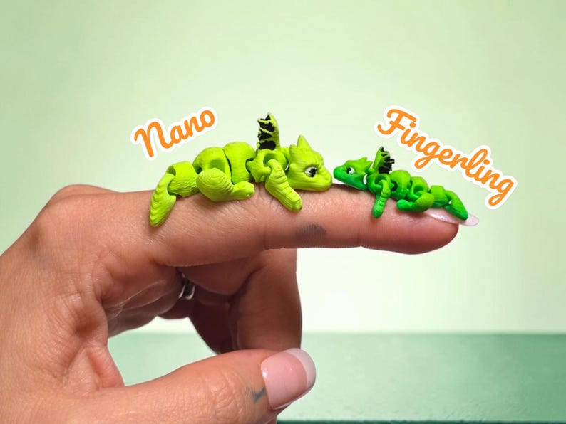 May include: Two small articulated dragon figurines in bright green with black wing details. The larger dragon is labeled Nano and the smaller one is labeled Fingerling. Both figures feature segmented bodies and are positioned on a finger.