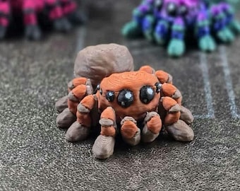 May include: A detailed, orange and brown spider figurine with large, expressive eyes. The spider has eight legs and a textured body, with a rounded head. Other spider figurines are blurred in the background.