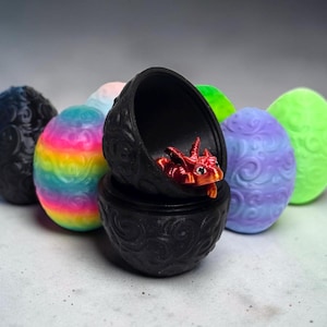 May include: A collection of oval-shaped containers with embossed swirl patterns in various colors, including black, rainbow, purple, and neon green. One black container is open, revealing a small, metallic red dragon figurine inside.