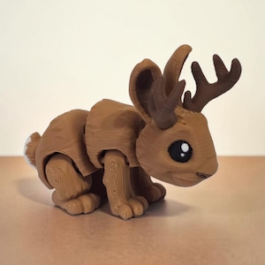 May include: A brown, articulated jackalope figurine with deer antlers and large, black eyes. The toy has a segmented body and a small, white tail. The figurine is posed in a crouching position.