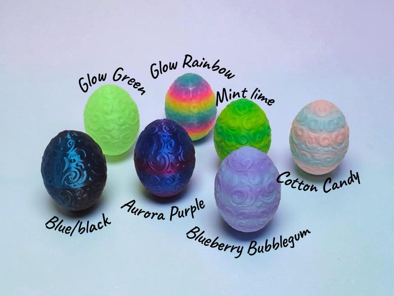 May include: Seven egg-shaped objects with embossed swirl patterns. Colors include Glow Green, Glow Rainbow, Mint Lime, Cotton Candy, Blue/Black, Aurora Purple, and Blueberry Bubblegum. Each egg is labeled with its corresponding color name in black text.