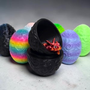May include: A collection of oval-shaped containers with embossed swirl patterns in various colors, including black, rainbow, purple, and neon green. One black container is open, revealing a small, metallic red dragon figurine inside.