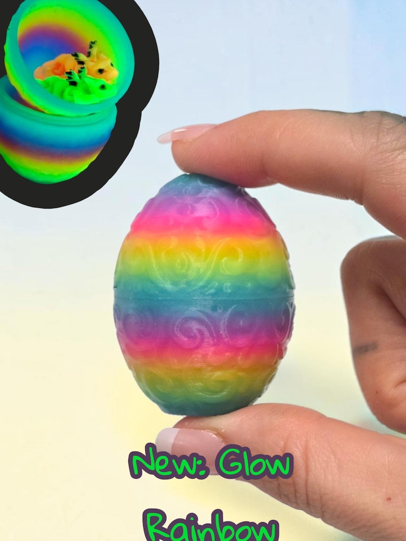 May include: A rainbow-colored egg with a raised swirl pattern. The egg is shown closed and also open in an inset, revealing a small, multi-colored creature inside. The text "New: Glow Rainbow" is printed in purple at the bottom of the image.