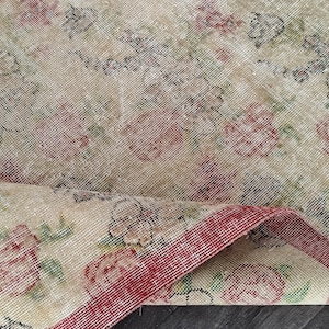 Puede incluir: Una alfombra vintage con un patrón floral en tonos rosa, verde y beige. La alfombra tiene un borde rojo y está doblada por la mitad.