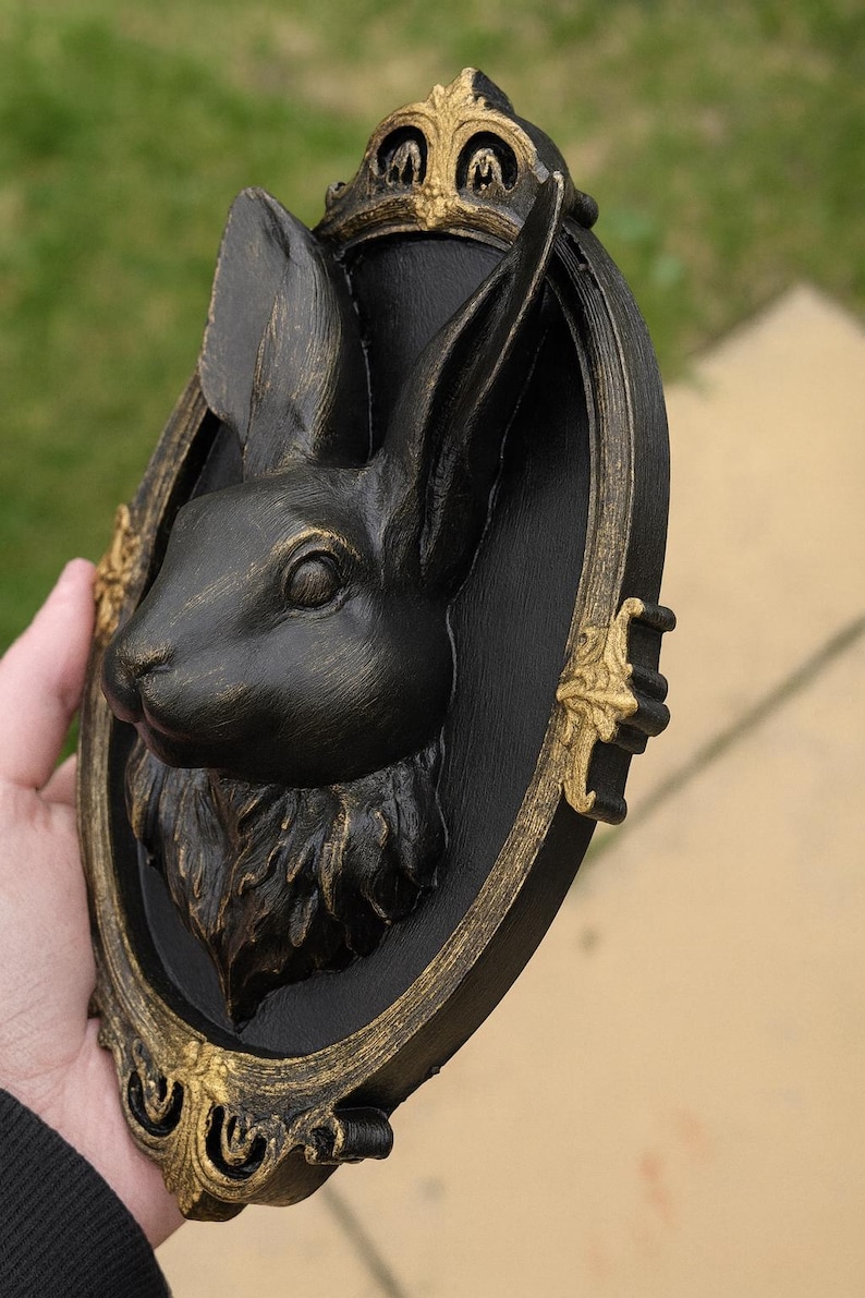 Peut inclure: D&eacute;coration murale t&ecirc;te de lapin noire dans un cadre ovale avec des accents dor&eacute;s. Le lapin est sculpt&eacute; avec des d&eacute;tails de fourrure et pr&eacute;sente une couronne royale. Le cadre a des d&eacute;tails dor&eacute;s orn&eacute;s, cr&eacute;ant une esth&eacute;tique vintage.