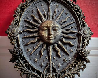 Op de afbeelding: Een ovaal wandbord met een centraal zonnegezicht met gesloten ogen en stralende stralen. Het donkere oppervlak is geaccentueerd met gouden details en kleine stermotieven. Het frame is versierd met krulwerk en drie gebeeldhouwde rozen.