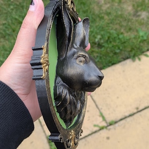 May include: Black rabbit head wall decor with a gold and black frame. The rabbit head is in profile, set against a green background. The frame has ornate gold detailing.