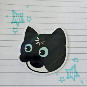 Può includere: Un adesivo a forma di gatto nero con muso bianco e occhi verde menta. L'adesivo ha un bordo bianco e un piccolo disegno a scoppio sulla fronte. Stelle verde menta sono disegnate attorno all'adesivo su uno sfondo di carta a righe.