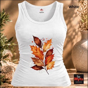May include: A white tank top featuring a central graphic of autumn leaves in shades of orange, red, and brown, accented with thin geometric lines and small red dots. The inner neck label displays the text Myts tapstich.