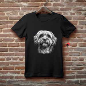 May include: Black t-shirt with a white and gray illustration of a dog's head. The dog has a fluffy, curly coat and is looking directly at the viewer.