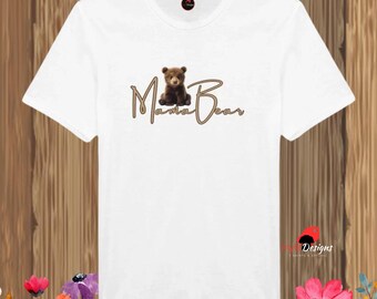 May include: White t-shirt with a brown bear graphic and the words "Mama Bear" in a cursive font. The shirt has a crew neck and short sleeves. The design is centered on the front of the shirt.