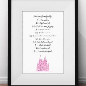 Puede incluir: Una impresión enmarcada en blanco con una ilustración rosa de la Catedral de Colonia y una lista de reglas escritas en alemán. El texto dice: "Kölsches Grundgesetz" seguido de una lista de reglas que comienzan con "§1-Et es wie et es" y terminan con "§11-Do laachste dech kapott".