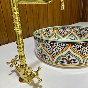May include: A gold faucet with two cross-shaped handles and a ceramic sink with a colorful Moroccan-inspired design.