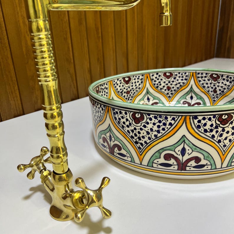 May include: A gold faucet with two cross-shaped handles and a ceramic sink with a colorful Moroccan-inspired design.